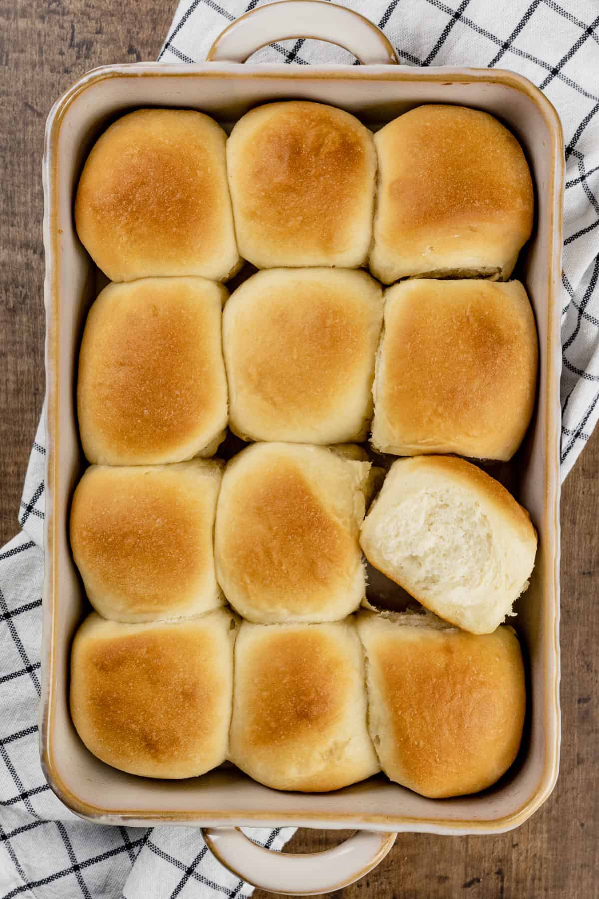 12 vegan dinner rolls after baking in a ceramic baking dish. One roll is turned on the side so you can see the fluffy texture.