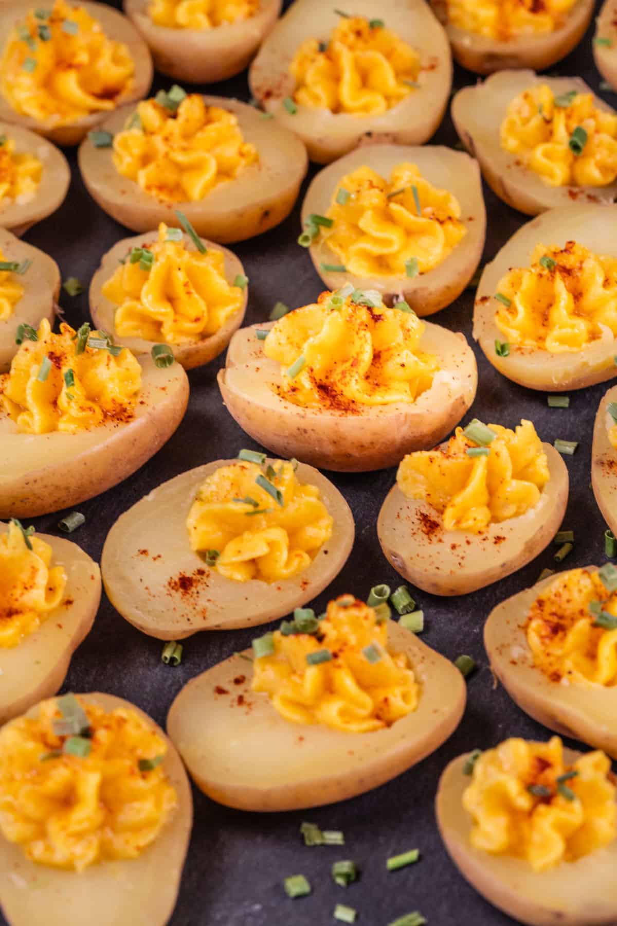 Side view of many vegan deviled potatoes filled with the filling and sprinkled with paprika and chives.