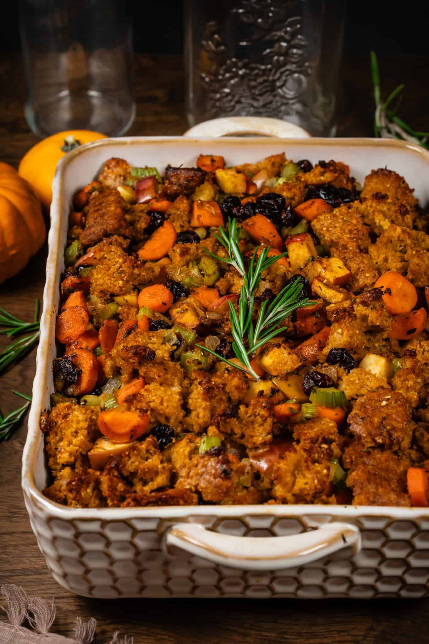 Closeup of vegan cornbread stuffing in a rectangle baking dish on a table with mini pumpkins and fresh rosemary sprigs.