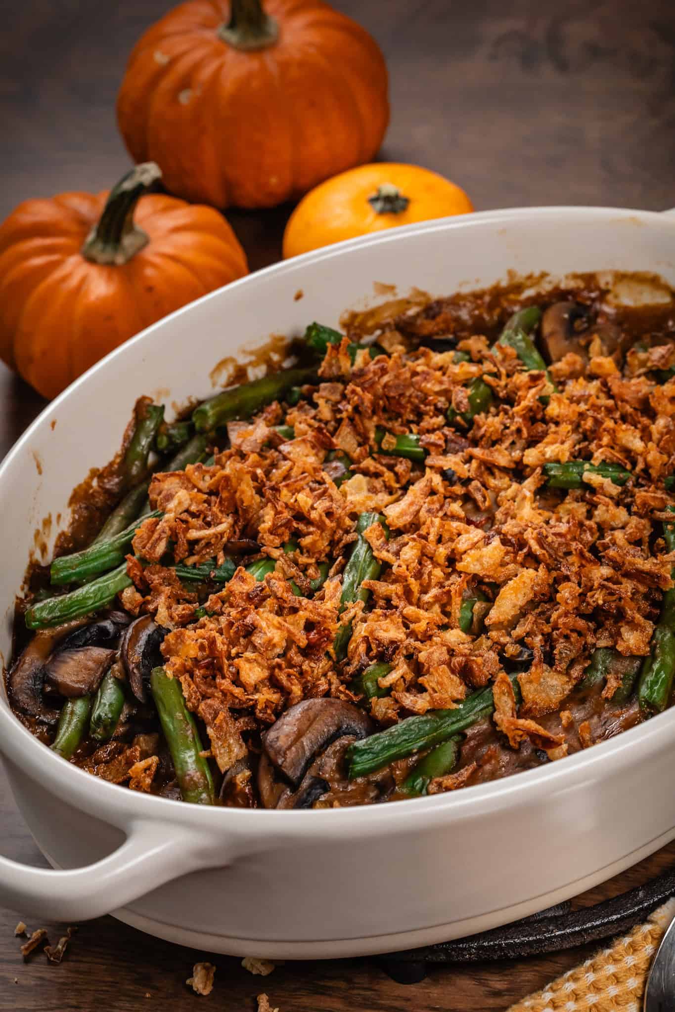 Side view of the vegan green bean casserole in an oval serving dish on the table with 3 mini pumpkins.